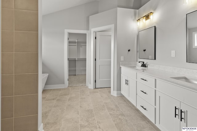 full bath featuring a freestanding bath, double vanity, a sink, and a walk in closet