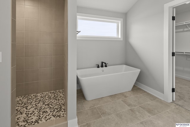 bathroom with a spacious closet, tiled shower, a soaking tub, and baseboards