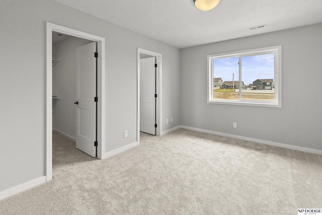 unfurnished bedroom with baseboards, a closet, a spacious closet, carpet flooring, and visible vents