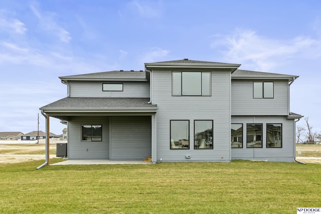 rear view of house with a patio area, cooling unit, a lawn, and roof with shingles