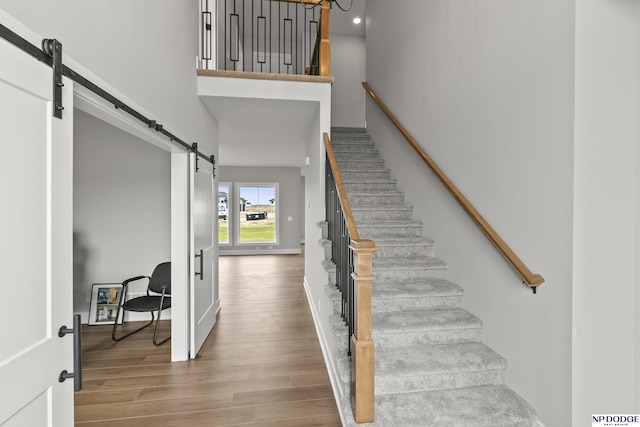 stairway with baseboards, a towering ceiling, a barn door, and wood finished floors