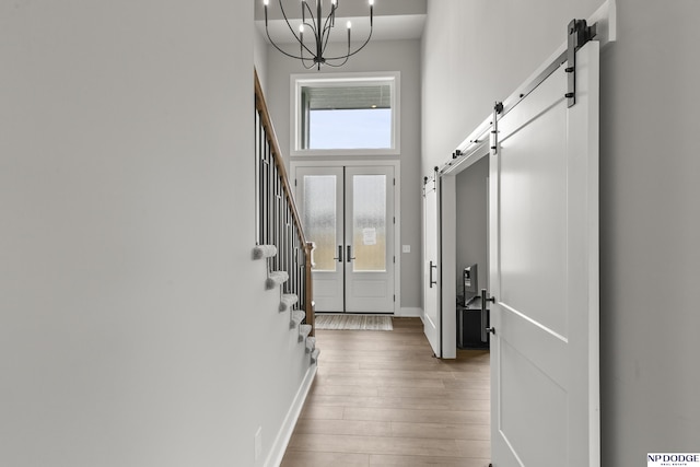 foyer featuring a notable chandelier, a high ceiling, stairs, a barn door, and wood finished floors