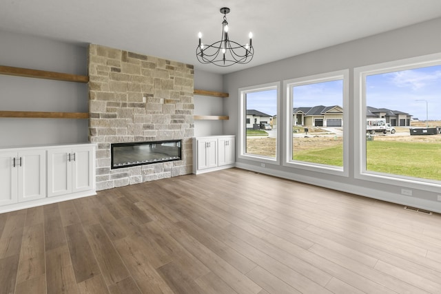 unfurnished living room with visible vents, a stone fireplace, an inviting chandelier, and wood finished floors