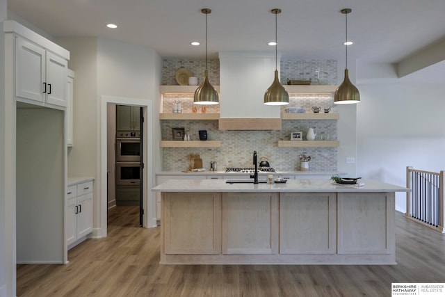 kitchen featuring white cabinetry, light hardwood / wood-style floors, pendant lighting, and a kitchen island with sink