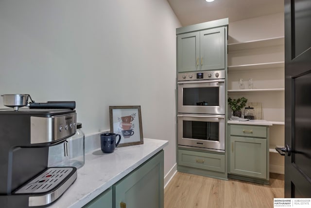 kitchen featuring light hardwood / wood-style floors, double oven, green cabinets, and light stone countertops