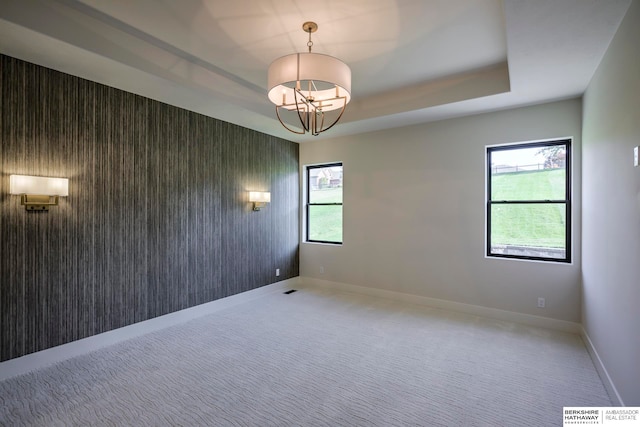 spare room featuring carpet, a tray ceiling, and an inviting chandelier