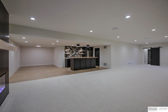 basement with light hardwood / wood-style floors, a barn door, and indoor bar