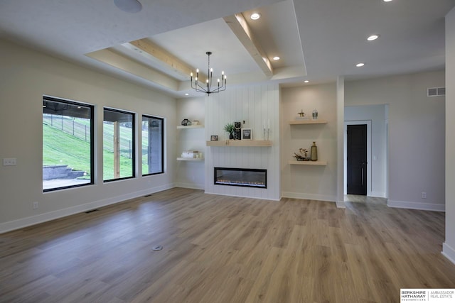 unfurnished living room with a notable chandelier, a tray ceiling, a large fireplace, and light wood-type flooring