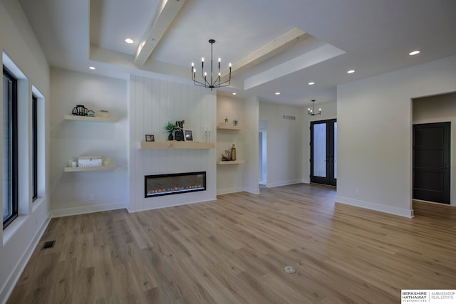 unfurnished living room featuring beam ceiling, a tray ceiling, a fireplace, light hardwood / wood-style floors, and a notable chandelier