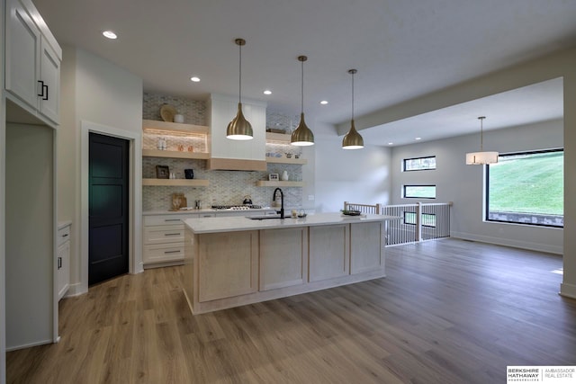 kitchen featuring light hardwood / wood-style floors, white cabinets, decorative light fixtures, and a center island with sink