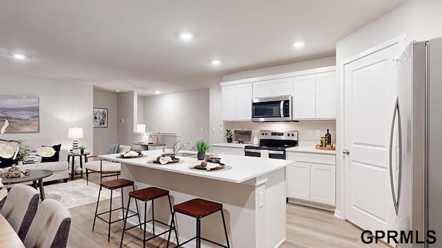 kitchen featuring appliances with stainless steel finishes, a kitchen breakfast bar, white cabinetry, a kitchen island with sink, and light hardwood / wood-style flooring