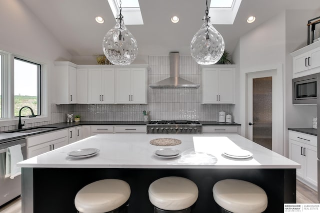 kitchen with a center island, stainless steel appliances, wall chimney exhaust hood, pendant lighting, and lofted ceiling with skylight