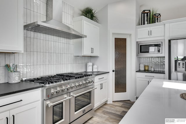 kitchen featuring wall chimney range hood, appliances with stainless steel finishes, and white cabinets