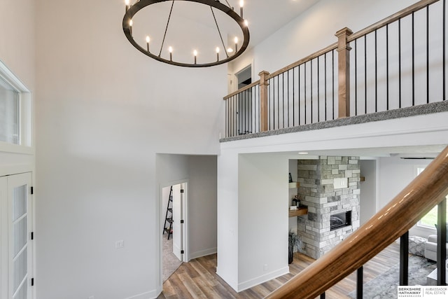 stairway with a towering ceiling, a notable chandelier, hardwood / wood-style flooring, and a stone fireplace