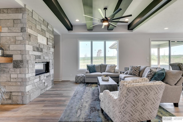 living room with a stone fireplace, wood-type flooring, a raised ceiling, and ceiling fan