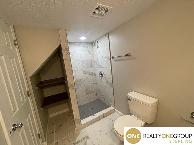 bathroom with toilet, a textured ceiling, and tiled shower