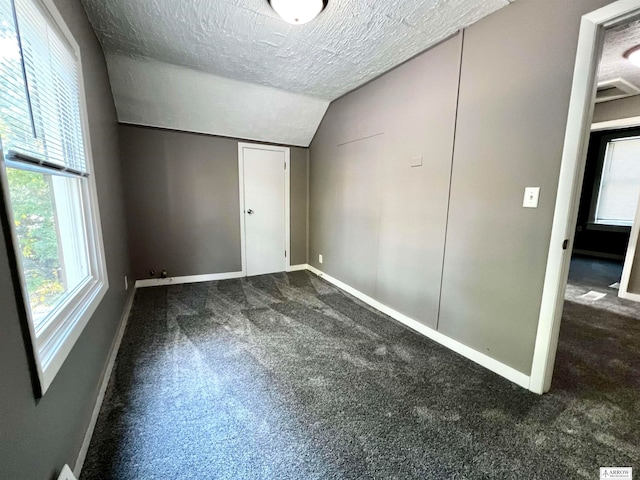 unfurnished bedroom featuring dark carpet, vaulted ceiling, multiple windows, and a textured ceiling