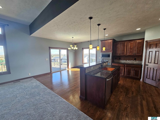 kitchen featuring appliances with stainless steel finishes, sink, pendant lighting, dark wood-type flooring, and a center island with sink