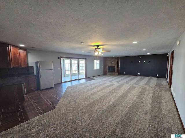 unfurnished living room featuring ceiling fan, a textured ceiling, and dark colored carpet