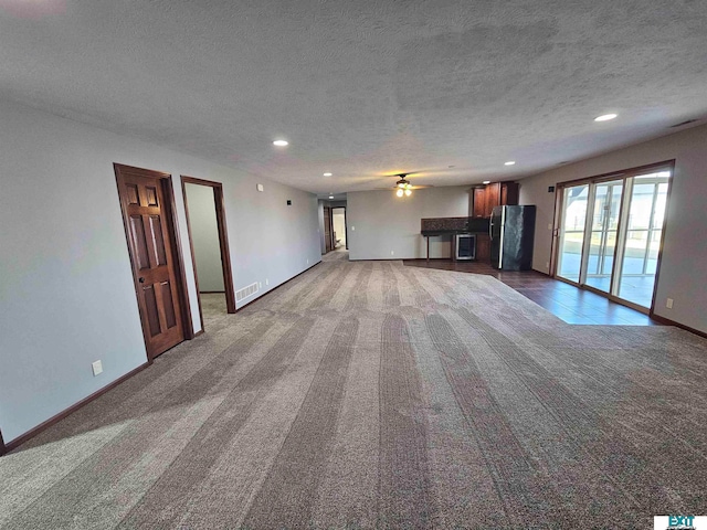 unfurnished living room with a textured ceiling, dark carpet, and ceiling fan