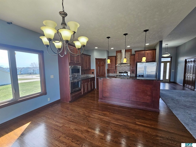 kitchen featuring dark hardwood / wood-style floors, wall chimney exhaust hood, stainless steel appliances, a center island with sink, and a notable chandelier