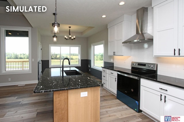 kitchen featuring a kitchen island with sink, sink, wall chimney range hood, white cabinets, and stainless steel range with electric cooktop