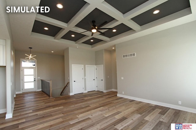 spare room with coffered ceiling, a towering ceiling, ceiling fan with notable chandelier, and hardwood / wood-style flooring