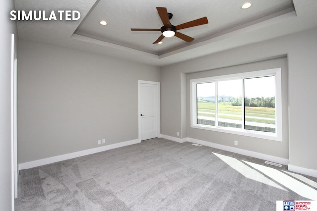 carpeted empty room with a raised ceiling and ceiling fan