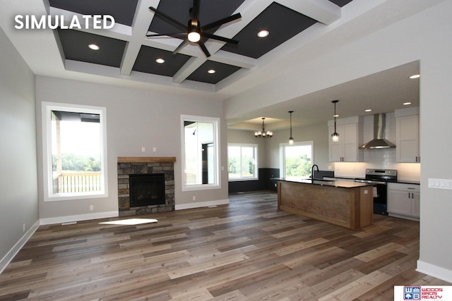 kitchen featuring wall chimney exhaust hood, electric range, decorative light fixtures, a center island with sink, and white cabinets