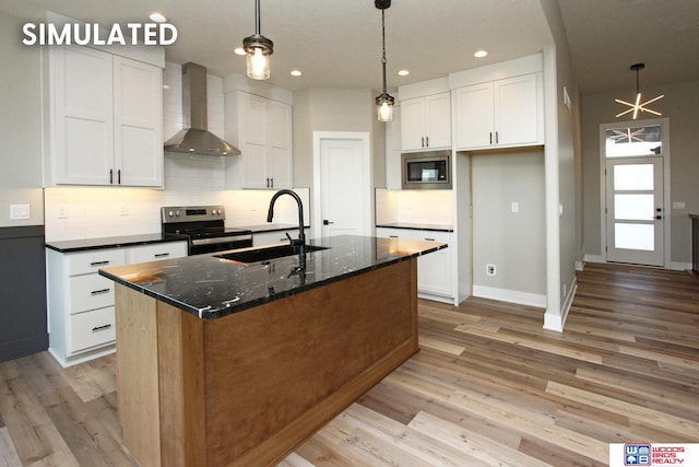 kitchen featuring appliances with stainless steel finishes, a kitchen island with sink, sink, wall chimney range hood, and white cabinets