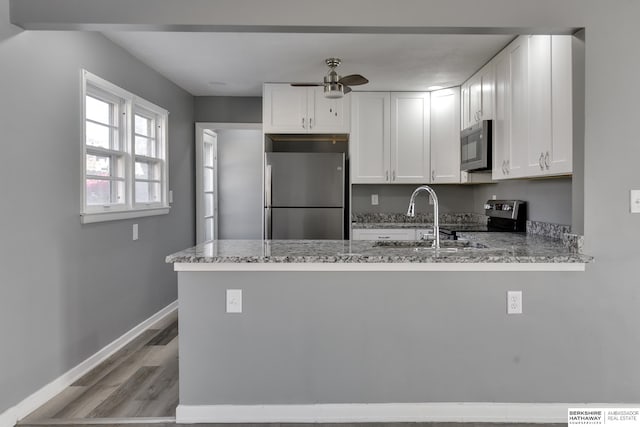 kitchen featuring light stone countertops, white cabinets, kitchen peninsula, and stainless steel appliances