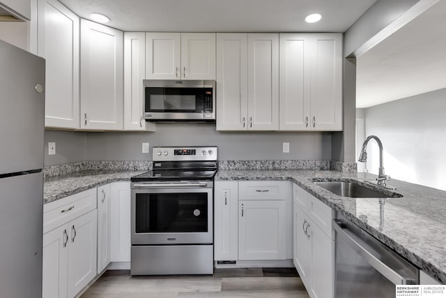 kitchen with stainless steel appliances, sink, white cabinetry, light stone counters, and light hardwood / wood-style floors