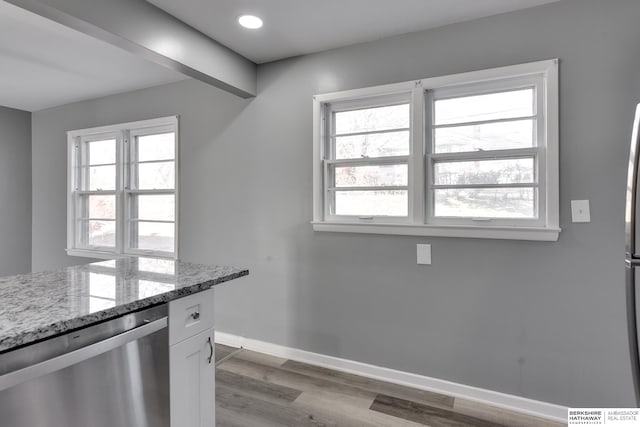 kitchen featuring white cabinetry, light stone countertops, stainless steel dishwasher, and a wealth of natural light