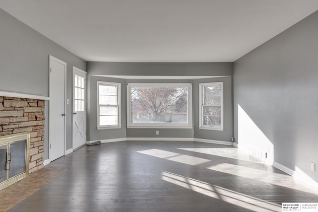 unfurnished living room featuring a stone fireplace and dark hardwood / wood-style floors