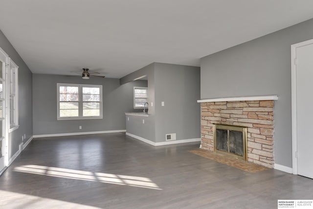 unfurnished living room featuring sink, ceiling fan, dark hardwood / wood-style flooring, and a fireplace