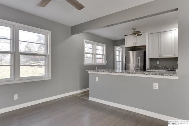 kitchen featuring stainless steel fridge, white cabinets, a healthy amount of sunlight, and light stone countertops