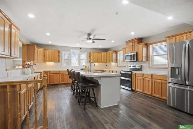 kitchen with a center island with sink, sink, a breakfast bar, appliances with stainless steel finishes, and dark hardwood / wood-style flooring