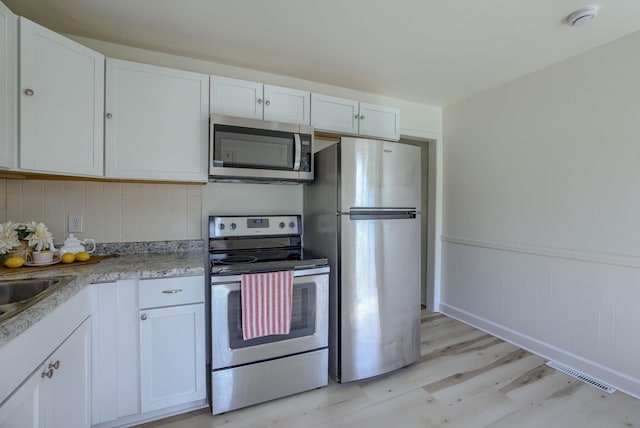 7336 S 71st Ave, Omaha, NE 68128 - kitchen featuring appliances with stainless steel finishes, light wood-style flooring, wainscoting, backsplash, and white cabinetry
