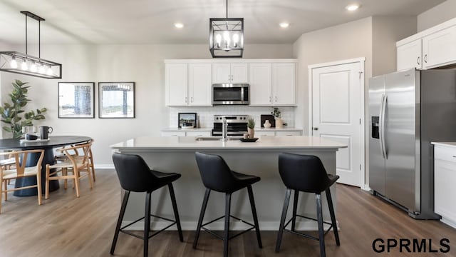 kitchen with appliances with stainless steel finishes, dark hardwood / wood-style flooring, and an island with sink