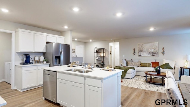 kitchen with appliances with stainless steel finishes, washing machine and clothes dryer, light hardwood / wood-style floors, white cabinets, and a kitchen island with sink