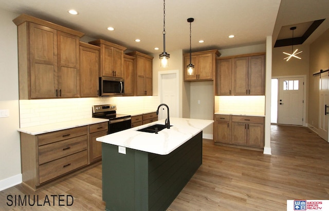 kitchen with an island with sink, a barn door, stainless steel appliances, sink, and decorative light fixtures