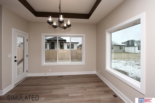 unfurnished dining area featuring hardwood / wood-style floors, a notable chandelier, and a tray ceiling