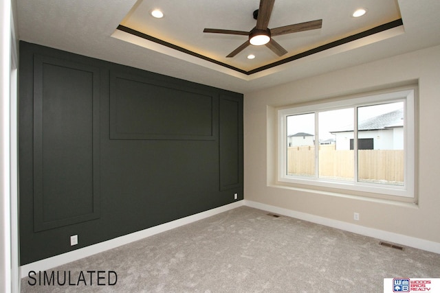 unfurnished room with ceiling fan, a tray ceiling, and light colored carpet