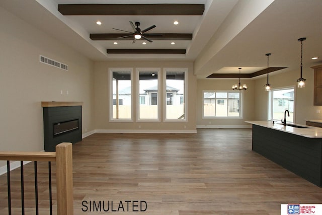 unfurnished living room with sink, ceiling fan with notable chandelier, light wood-type flooring, and a raised ceiling