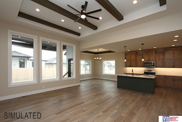 kitchen featuring a tray ceiling, a center island with sink, hardwood / wood-style floors, pendant lighting, and appliances with stainless steel finishes