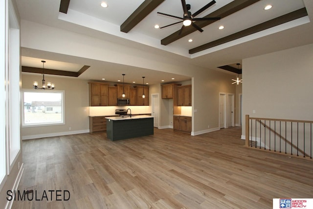 kitchen with a kitchen island with sink, hanging light fixtures, a tray ceiling, sink, and light wood-type flooring