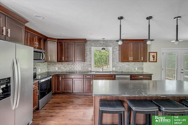 kitchen featuring dark wood-type flooring, appliances with stainless steel finishes, hanging light fixtures, and plenty of natural light