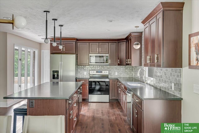 kitchen featuring appliances with stainless steel finishes, sink, a kitchen island, dark hardwood / wood-style flooring, and decorative light fixtures