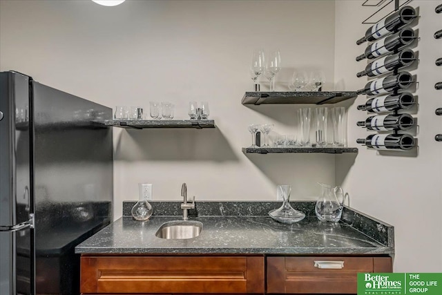 kitchen with dark stone countertops, sink, and black refrigerator