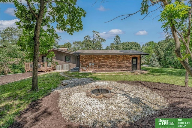 back of house with a wooden deck, a lawn, and a fire pit